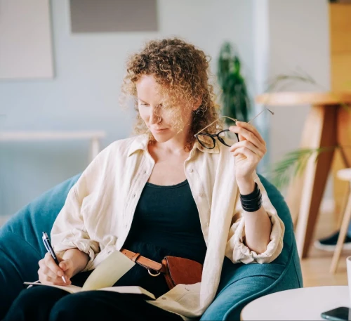 woman puts on glasses and writes in paper notebook e1665229594130