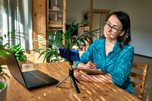 woman sitting by window in living room writing notes in her notebook freelance working